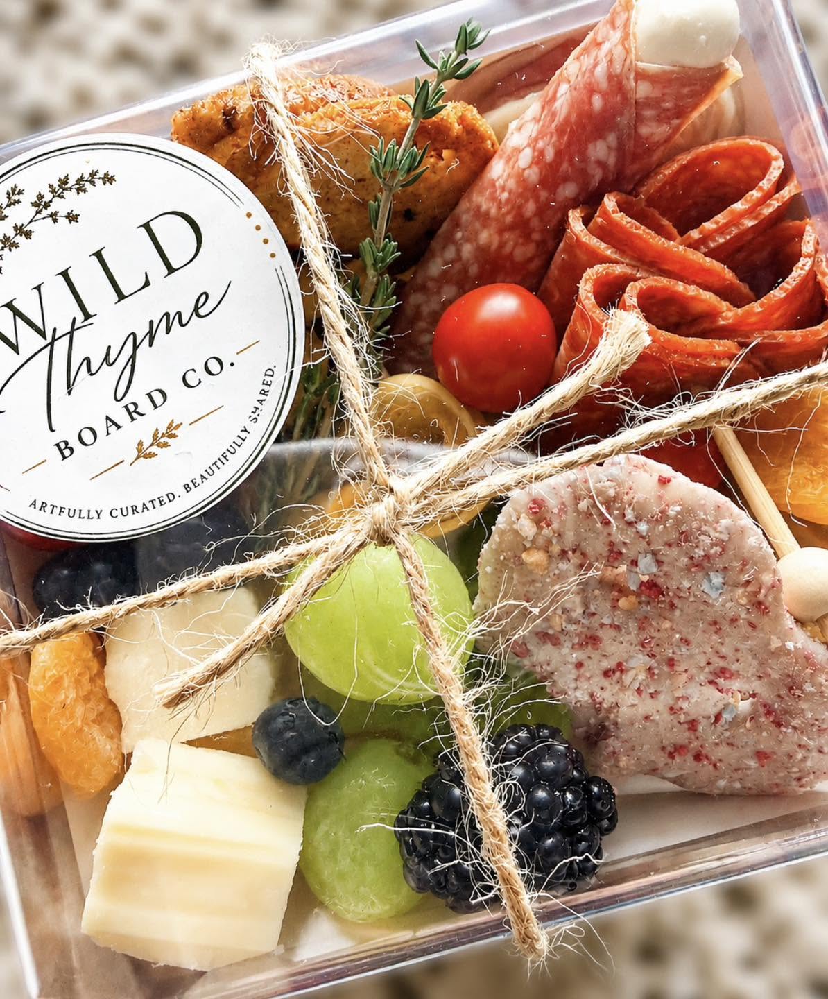 A Wild Thyme grazing box with salami roses, cheeses, fruit, and fresh thyme, tied with twine